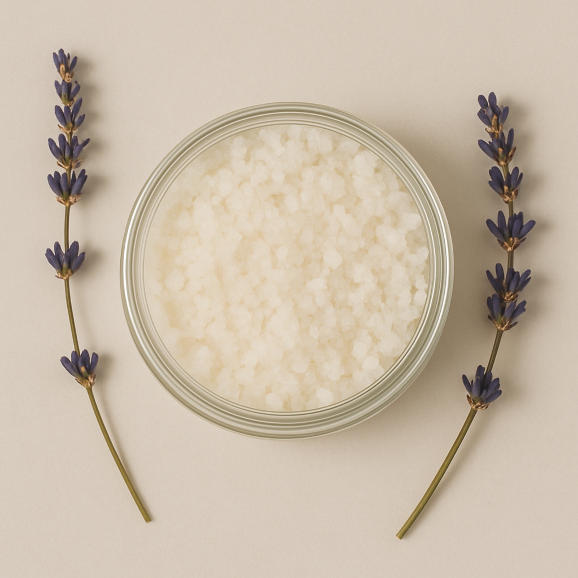 Overhead view of an open jar filled with white bath salts, centered on a neutral beige background, flanked by two sprigs of fresh lavender on either side. Our product does not include jar.