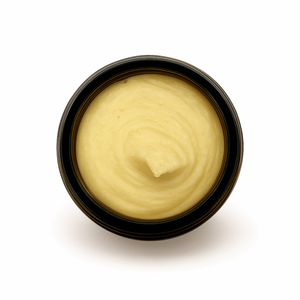 Top-down view of an open amber jar filled with whipped honey tallow balm for face & body, showing its smooth, creamy texture.